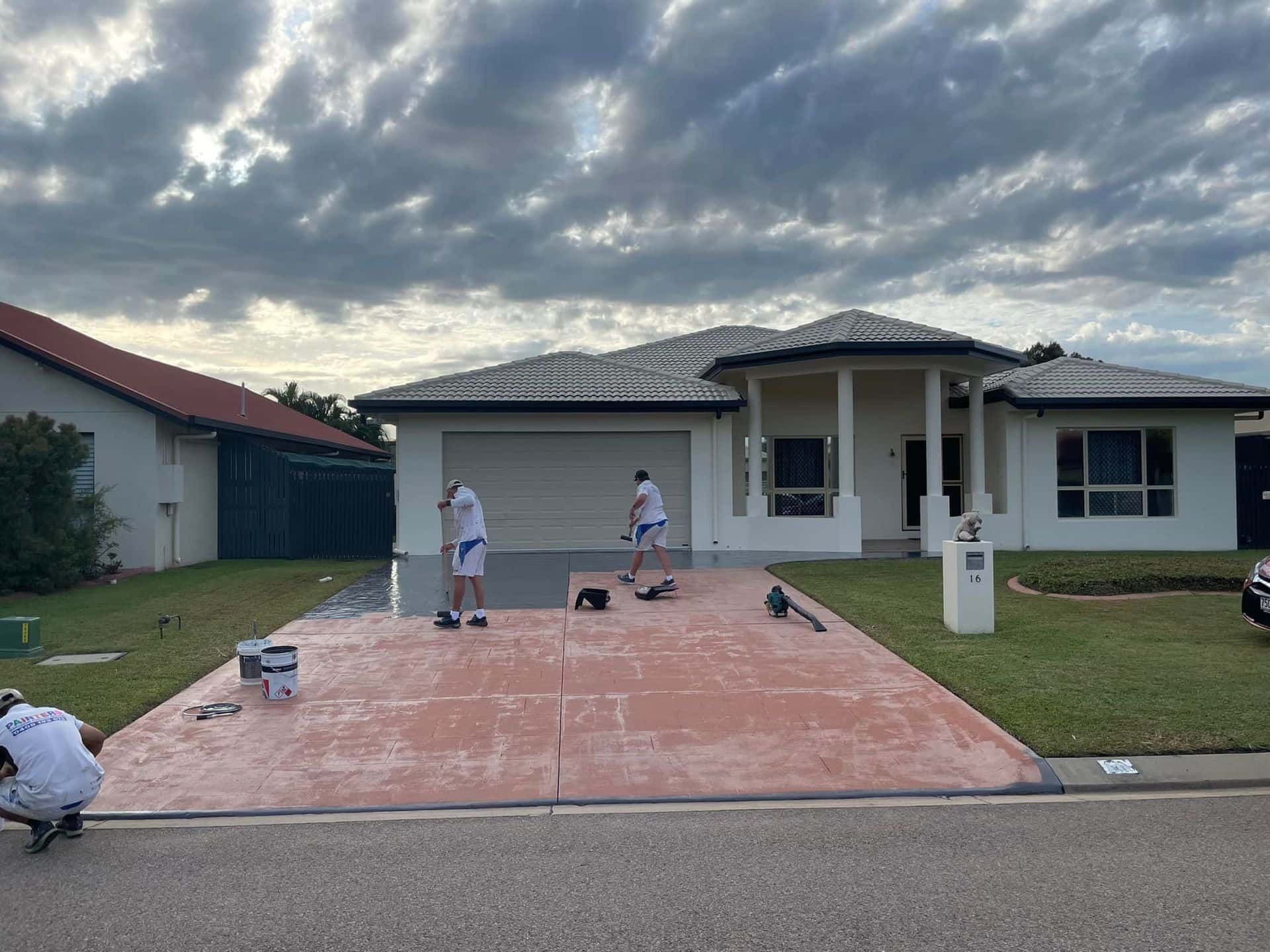 Two men are painting a driveway in front of a house.