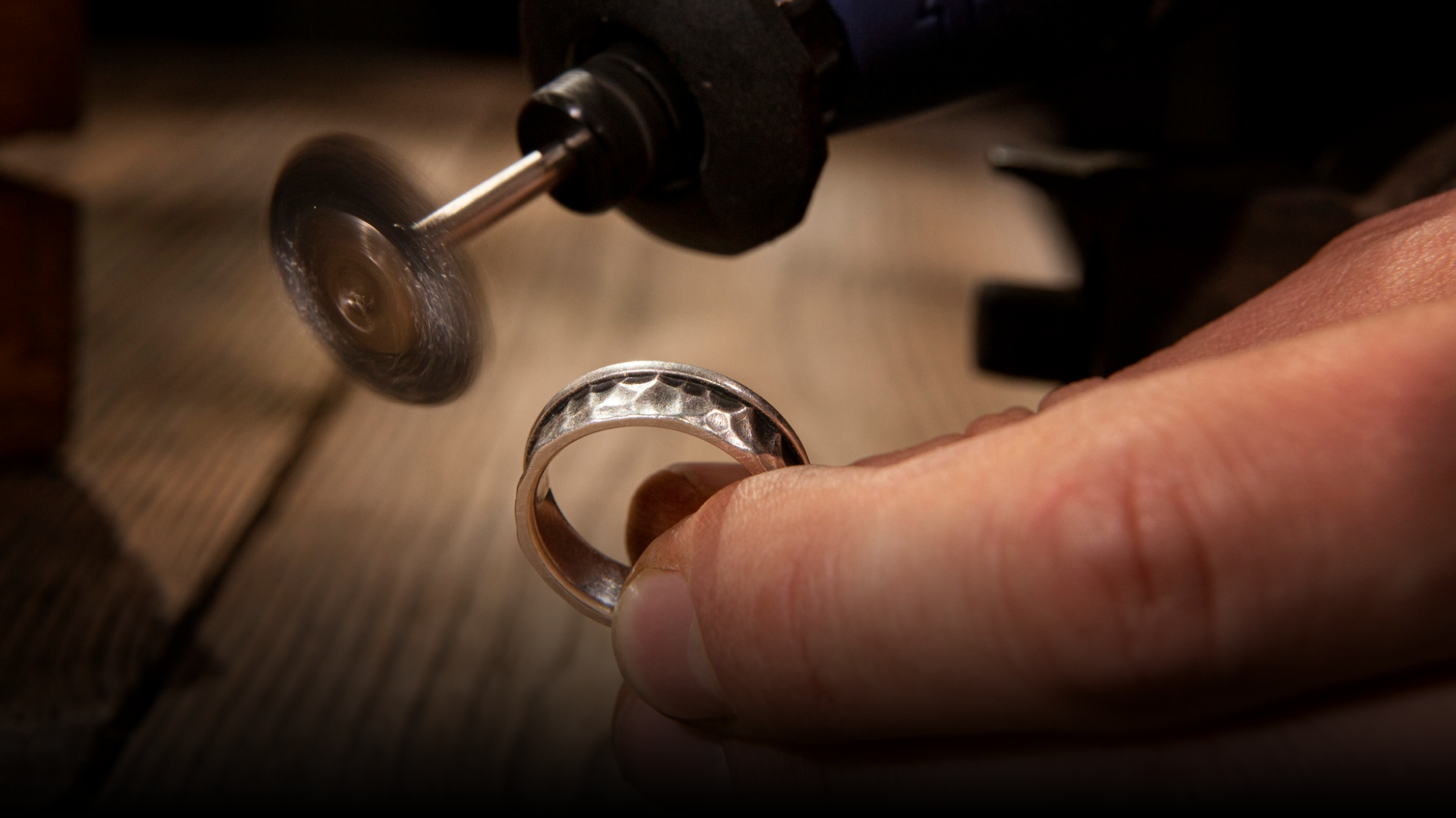 A person is polishing a silver ring with a machine.