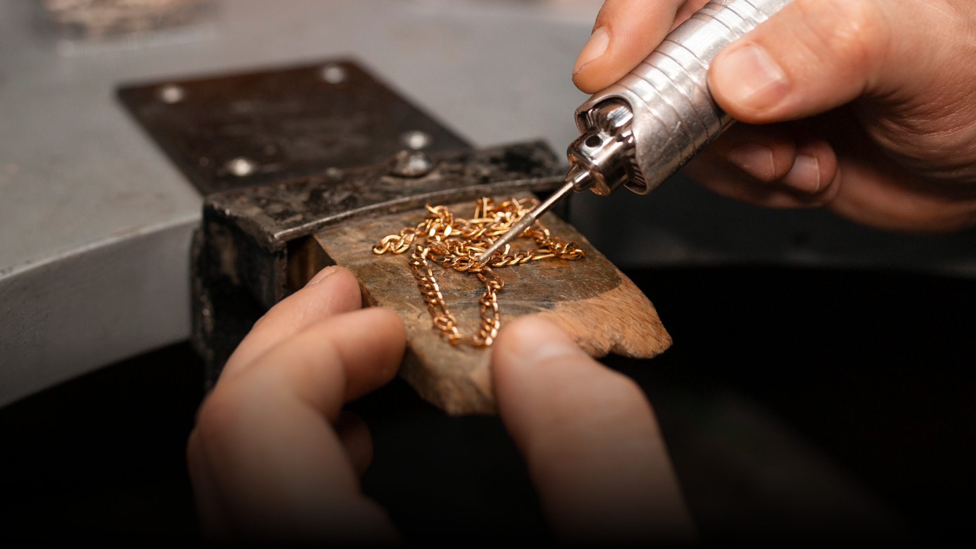 A person is working on a gold chain with a tool.