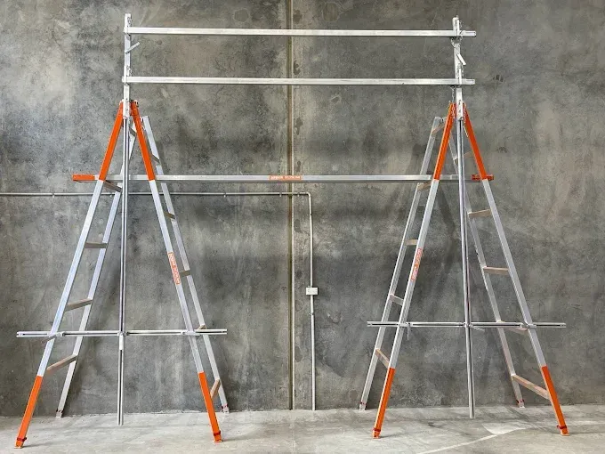 Two tall aluminum ladders connected by horizontal support poles to form a makeshift scaffolding structure against a wall — Superior Access Hire in Wynnum, QLD