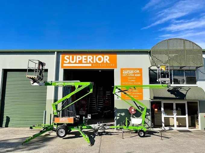Two green towable cherry picker lifts parked in front of a building with a
