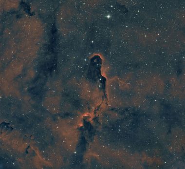 A dark, towering pillar of cosmic dust and gas stands out against a backdrop of glowing orange nebula and bright stars.