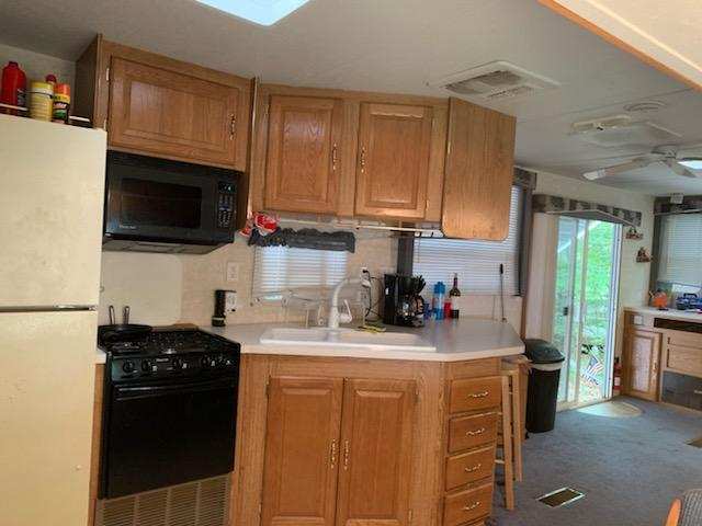 Kitchen interior with wooden cabinets, white countertops, black stove, and refrigerator near a sliding glass door.