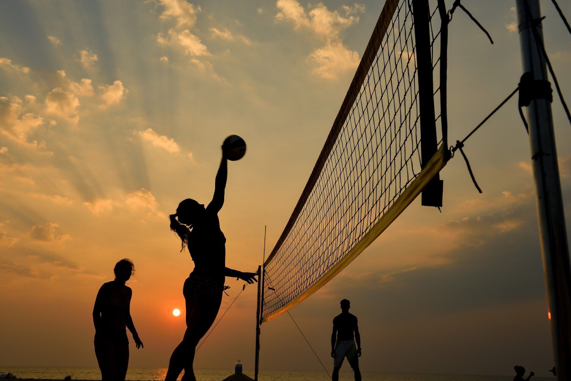 Beach volleyball at sunset; player spikes ball over net.