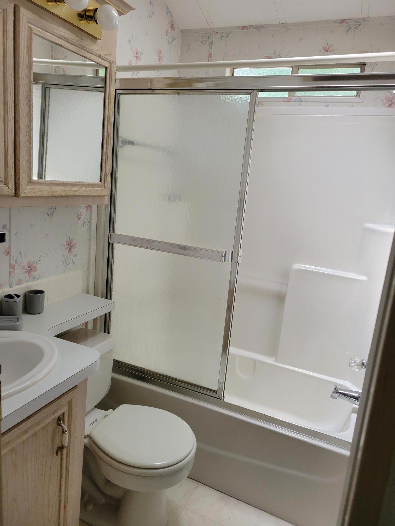 Bathroom with toilet, sink, tub, frosted sliding shower doors, and floral wallpaper.