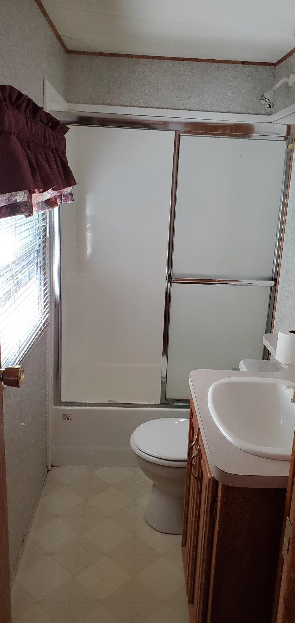 A small bathroom with a shower, toilet, and vanity. Beige and white tones dominate.