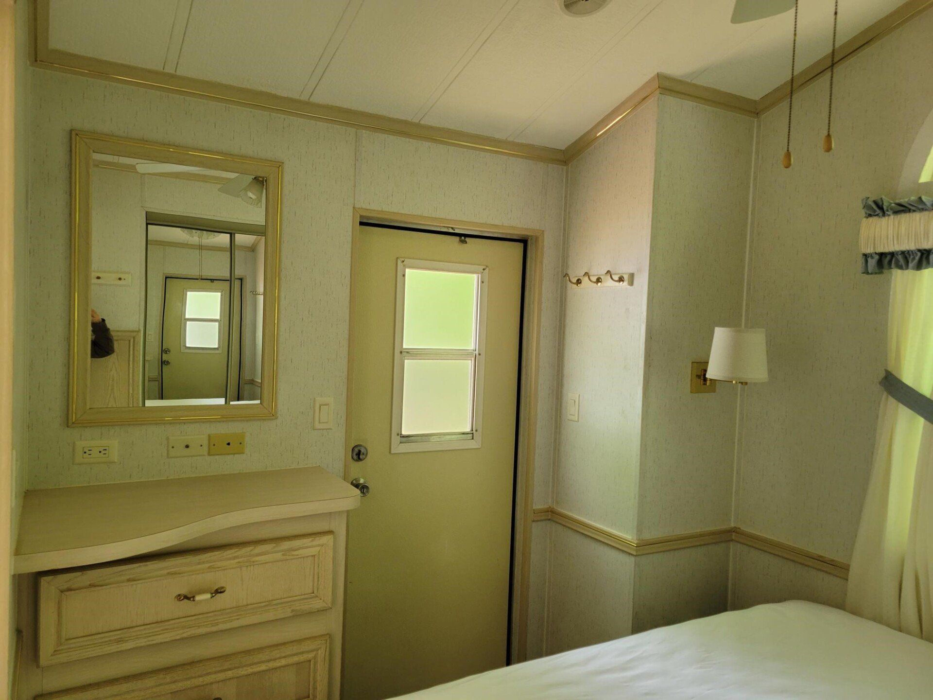 Bedroom interior with a bed, dresser, door, and mirror. Pale walls and trim.