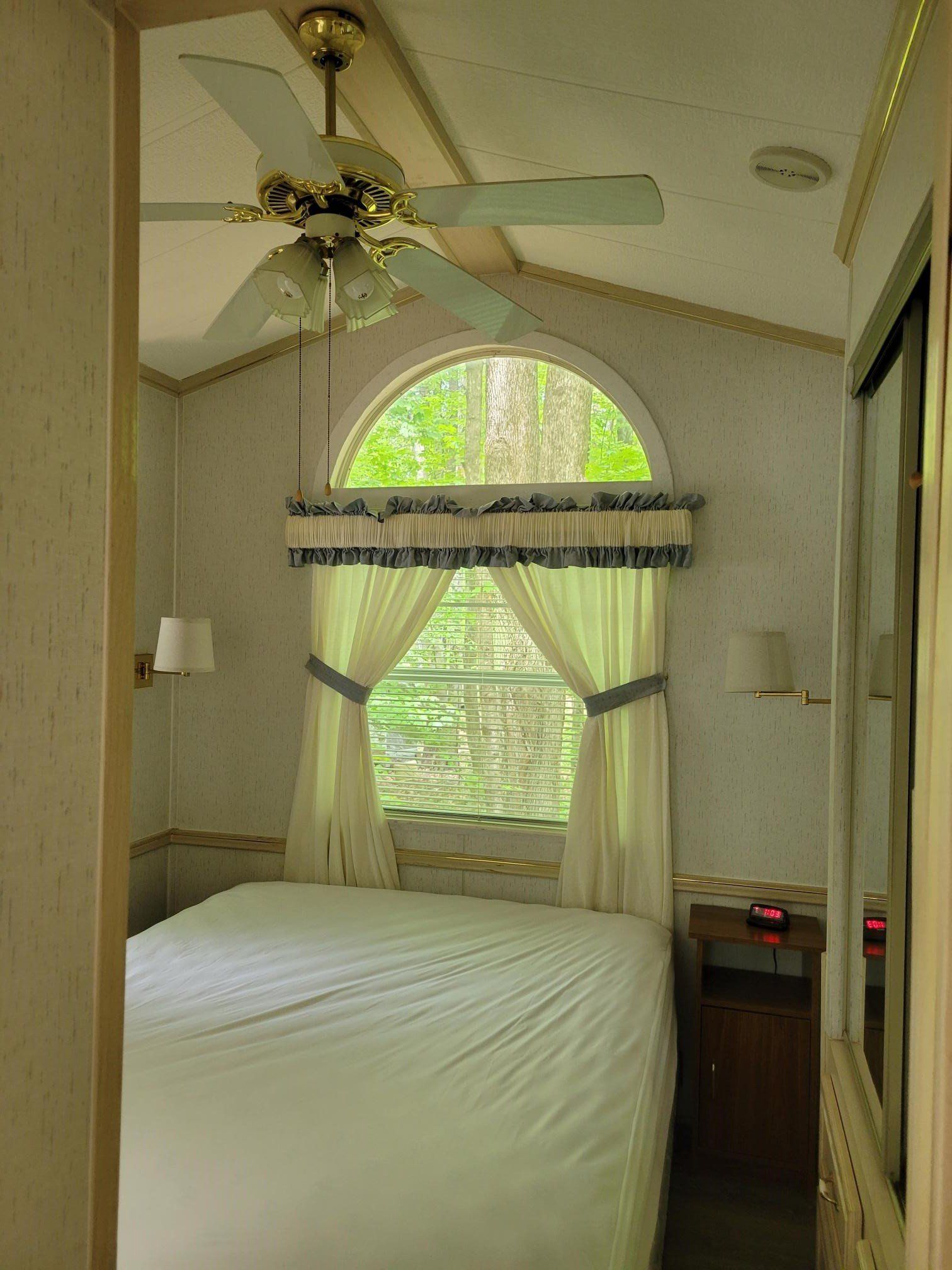 Bedroom interior with a bed, window with curtains, and ceiling fan.