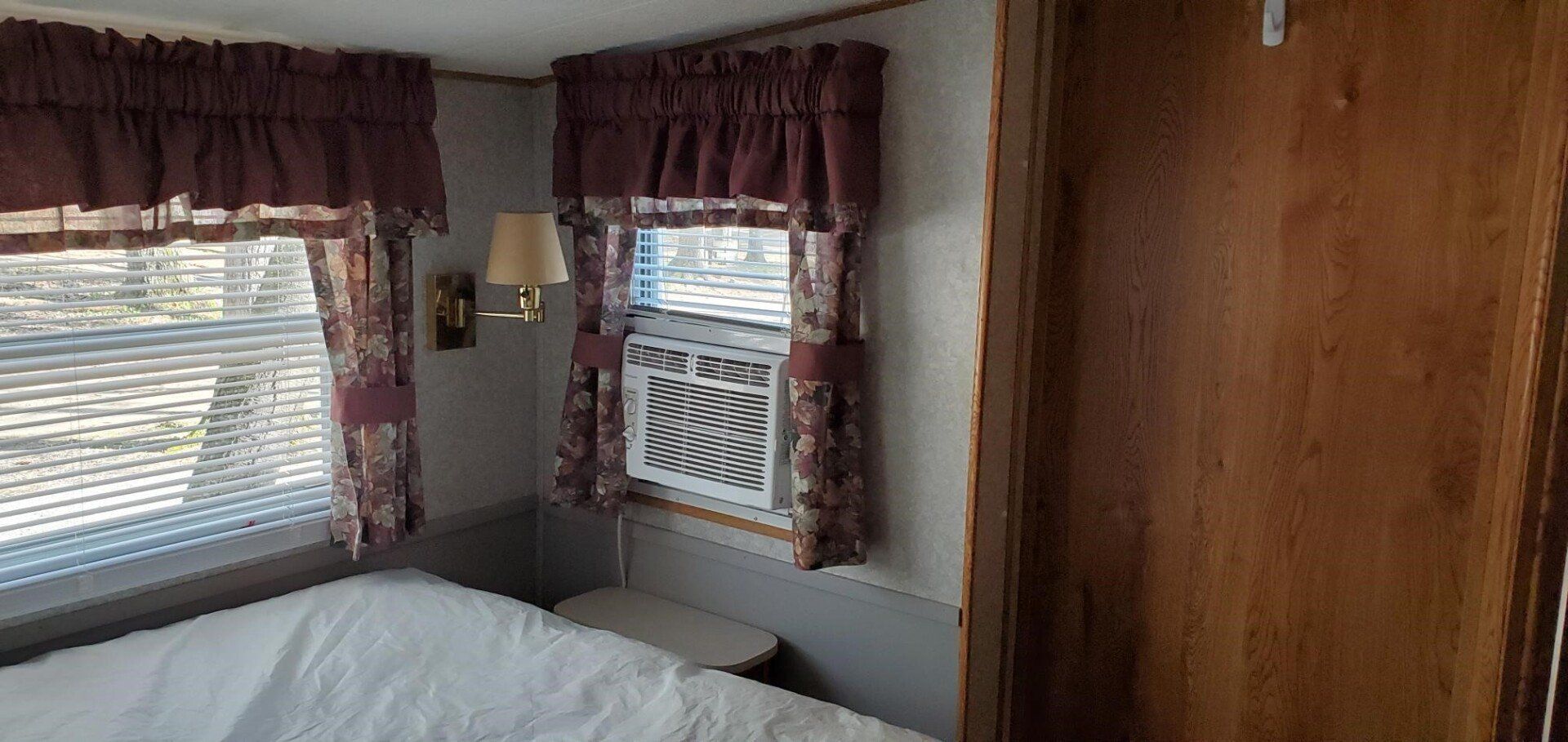 Bedroom interior with windows, burgundy curtains, air conditioner, and wooden door.