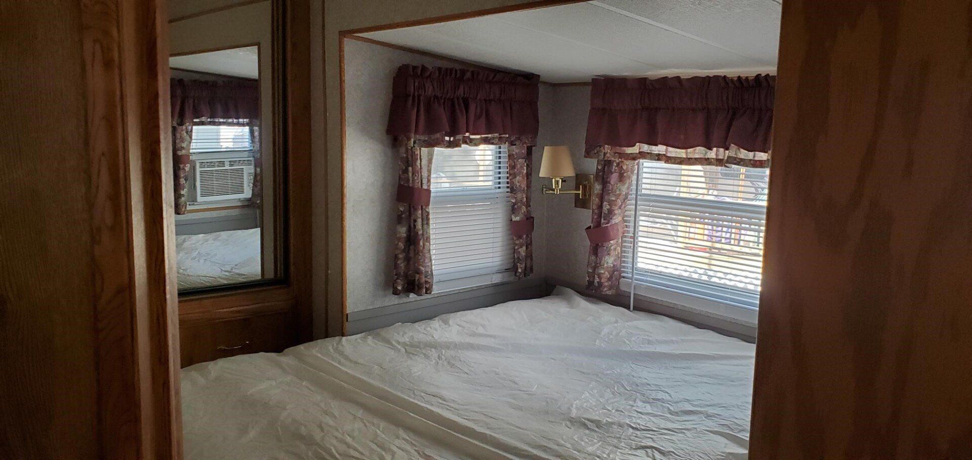 Bedroom with bed, windows, and drapes. A mirrored closet is visible on the left.