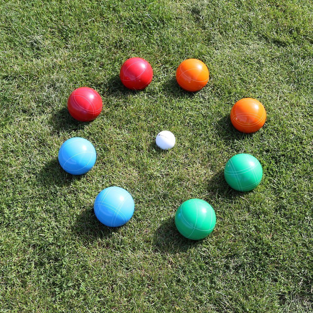 Bocce balls in a circle around a small white ball on a grass lawn; red, orange, blue, and green balls.