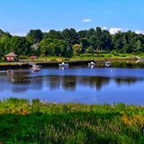 Blue lake with several boats and a forested shoreline under a bright blue sky.