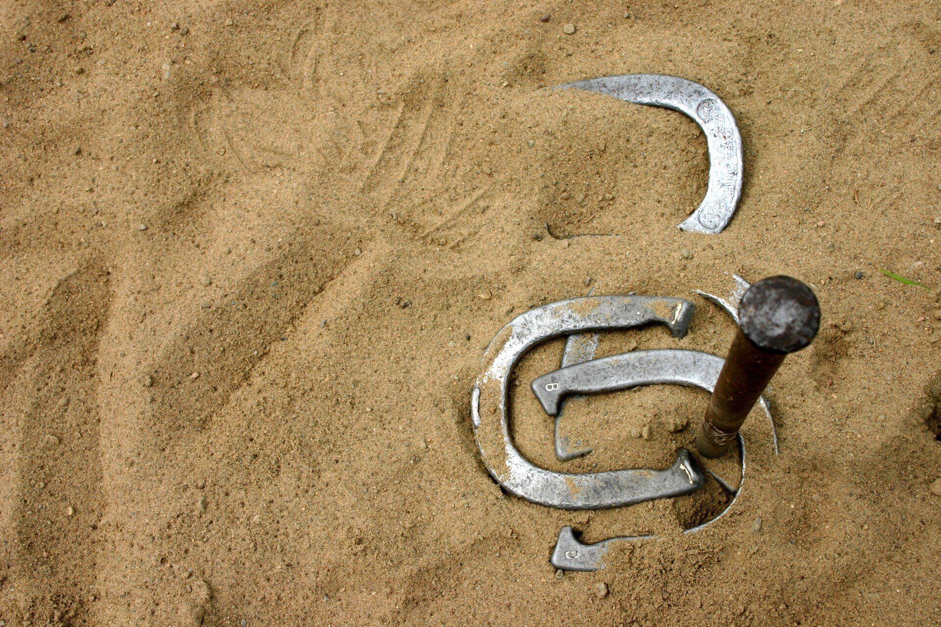 Horseshoe game: Horseshoes around a stake in sand. One complete ringer.
