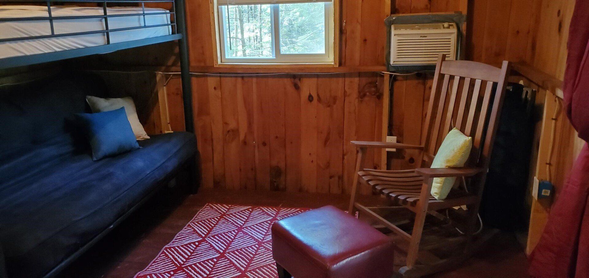 Cozy cabin interior with bunk bed, futon, rocking chair, and red patterned rug.