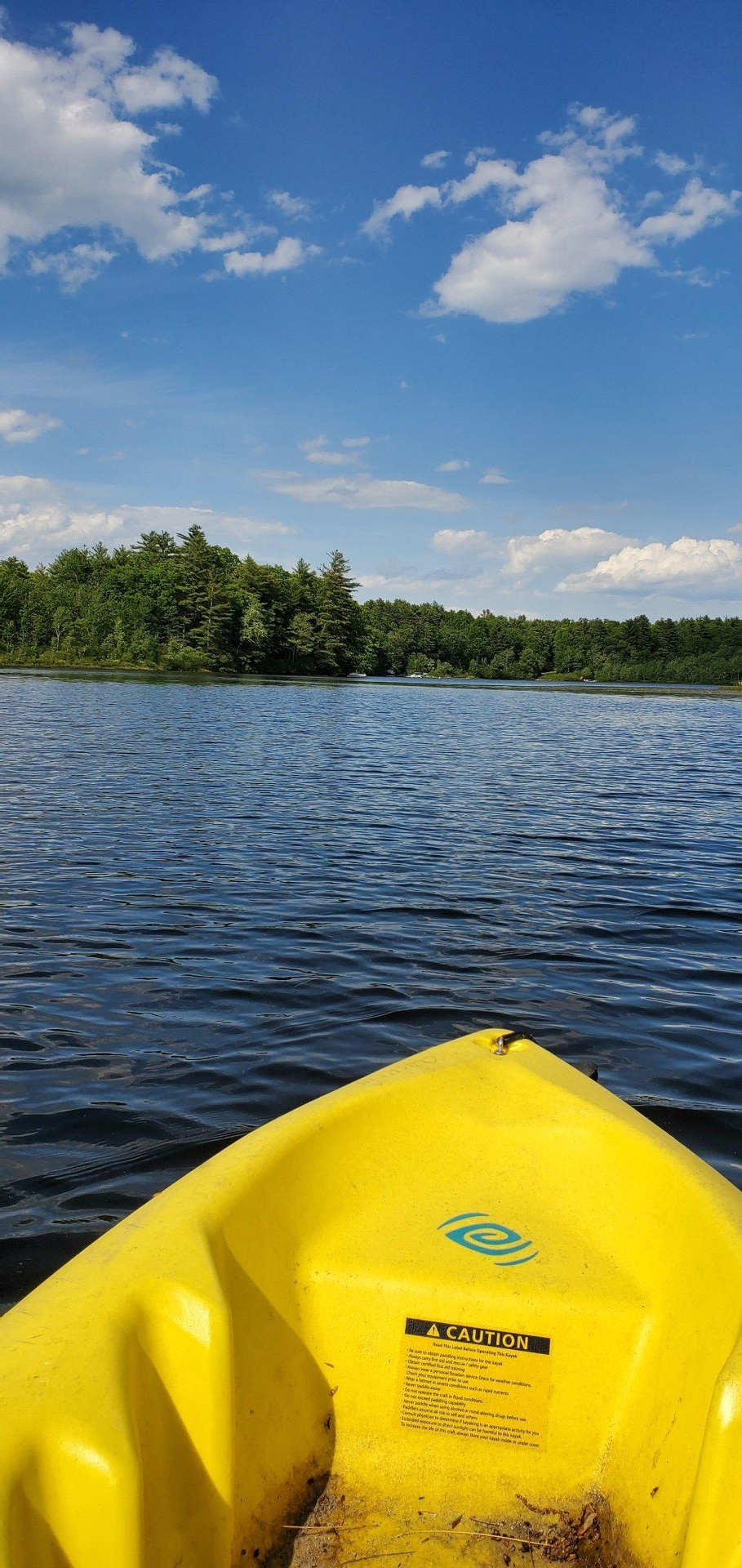 Yellow kayak on a lake with trees on the horizon under a blue sky with clouds.