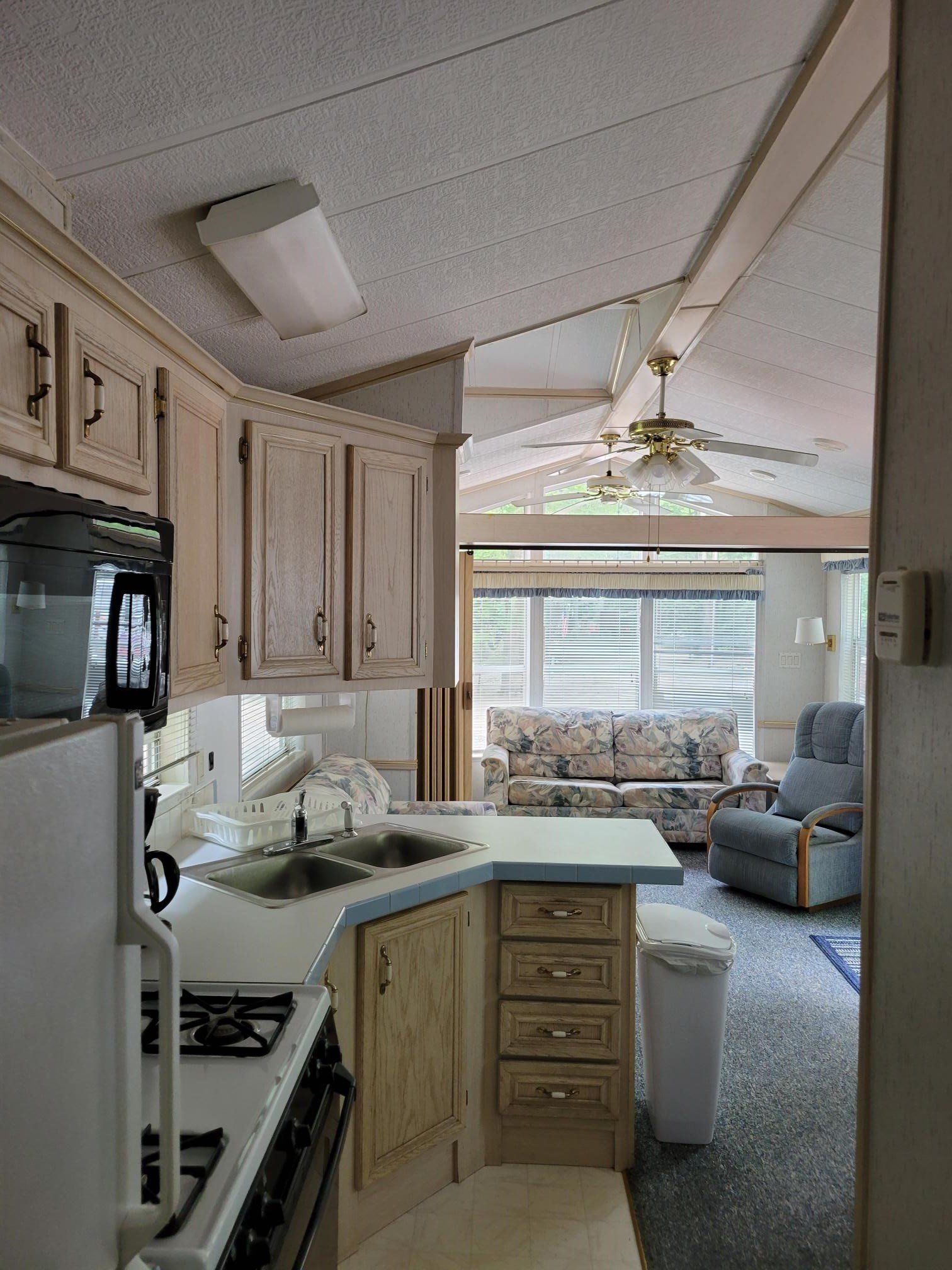 Interior of a trailer kitchen and living area, with light cabinets, a microwave, stove, and a sofa.