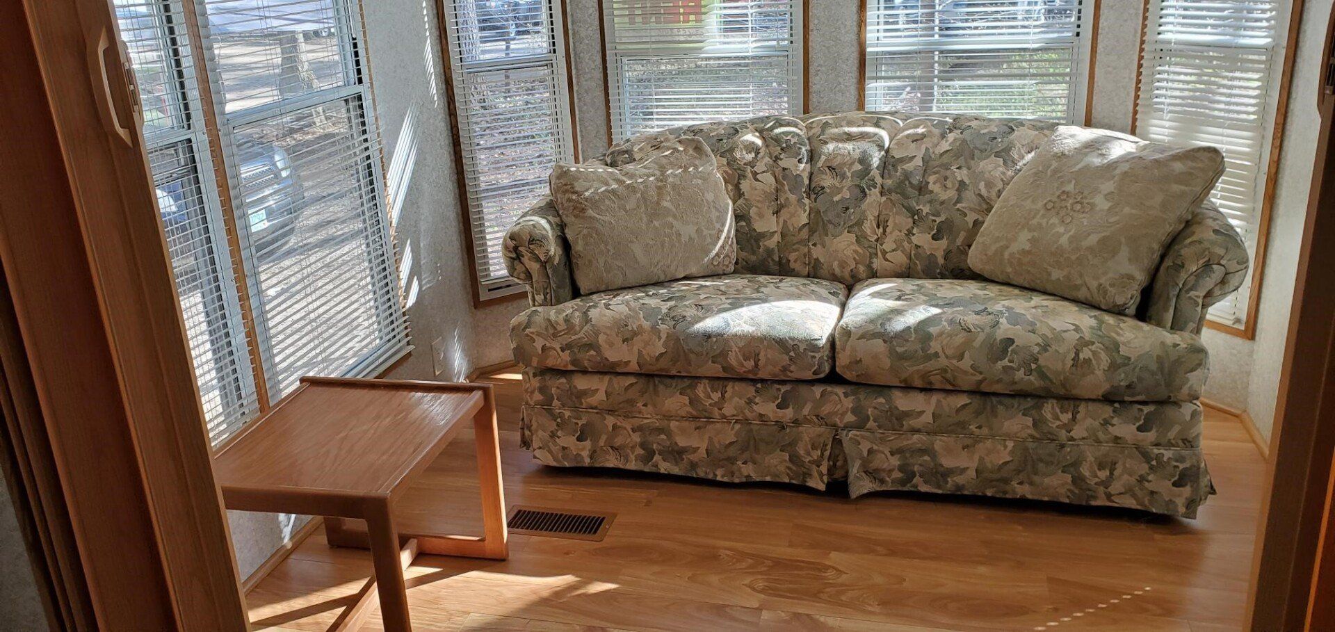 A living room with a patterned sofa, small wooden table, and windows letting in sunlight.