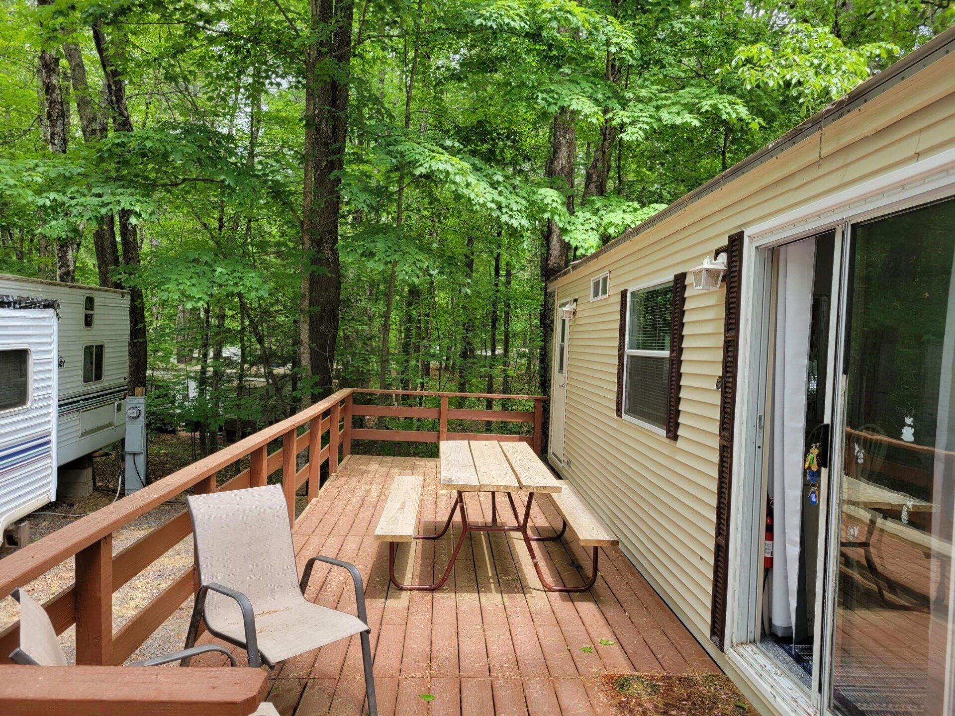 Deck with picnic table and chairs outside a cabin in a wooded area.