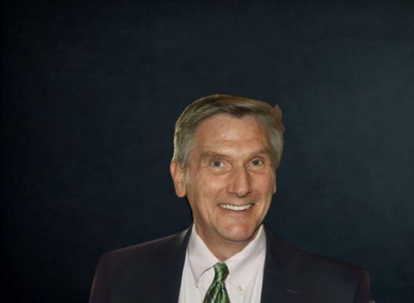 Portrait of a smiling man in a dark suit and green tie against a black background