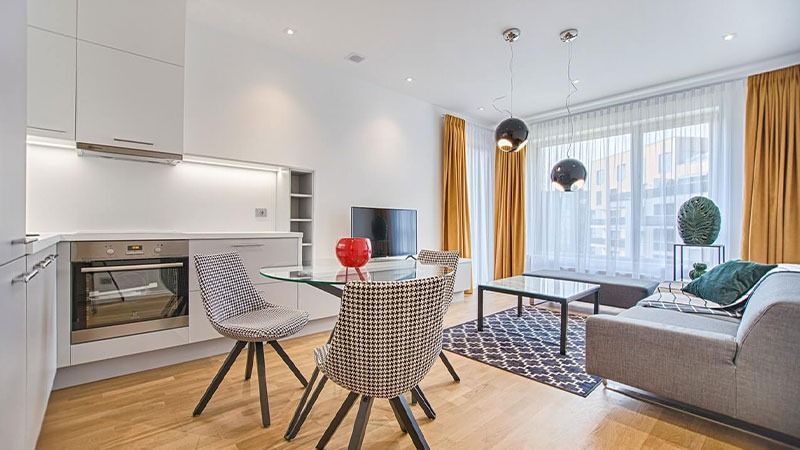 Modern open-plan living room with sofa, dining table, white kitchen, and large windows with yellow curtains