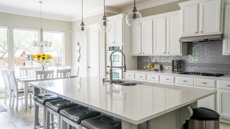 Bright white kitchen with island, bar stools, pendant lights, and dining area by large windows