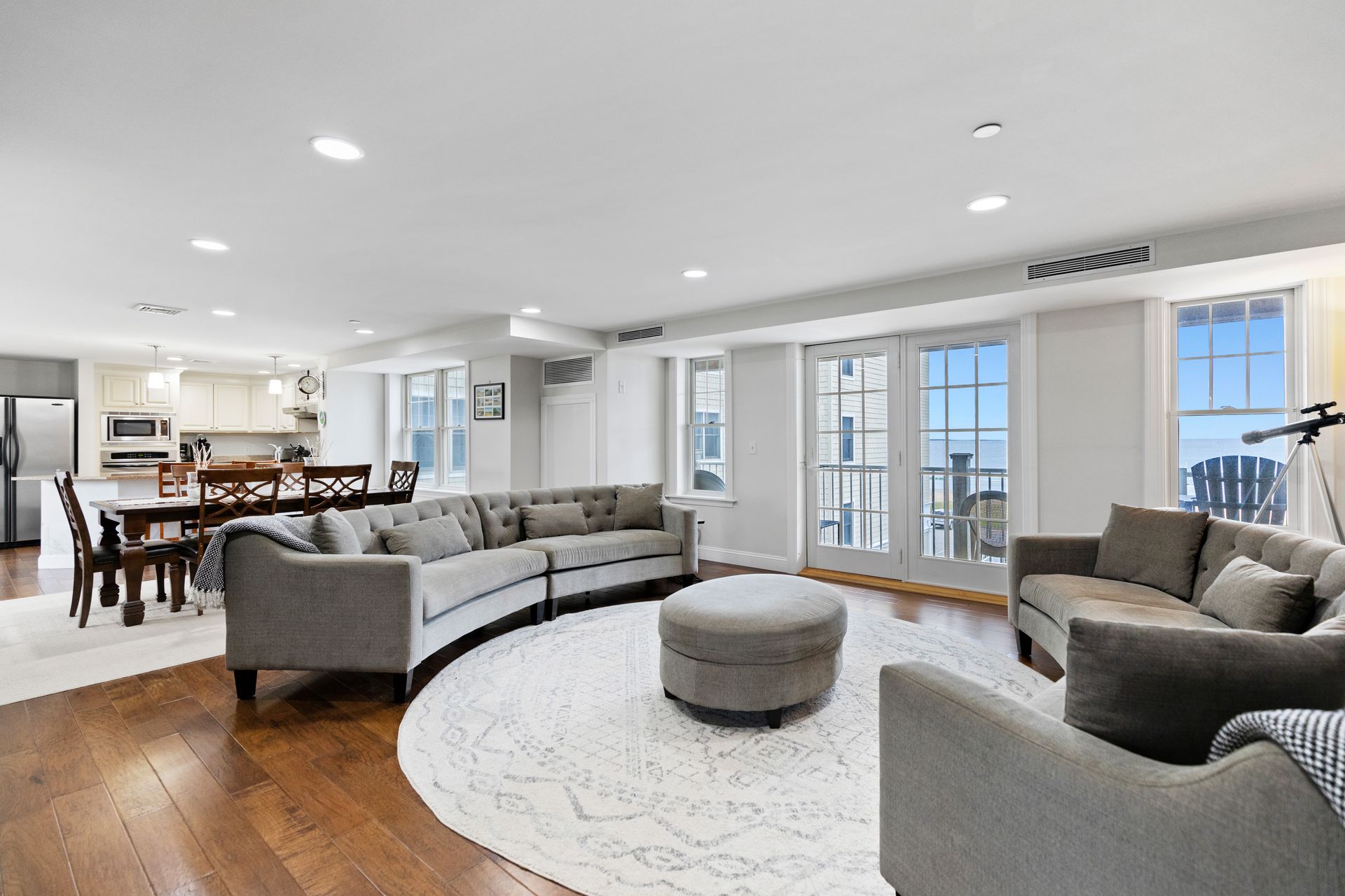 A living room with a large sectional couch , chairs , ottoman and dining table.