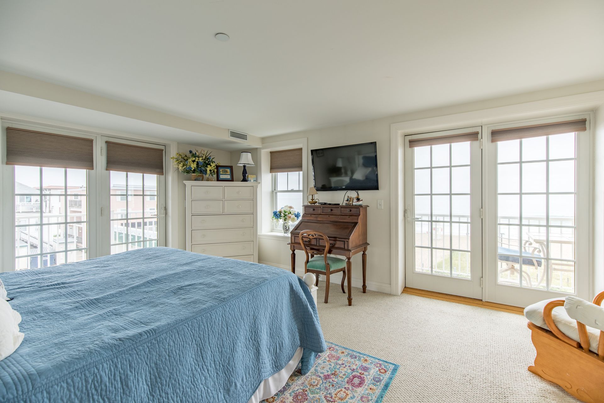 A bedroom with a large bed , desk , television and lots of windows.