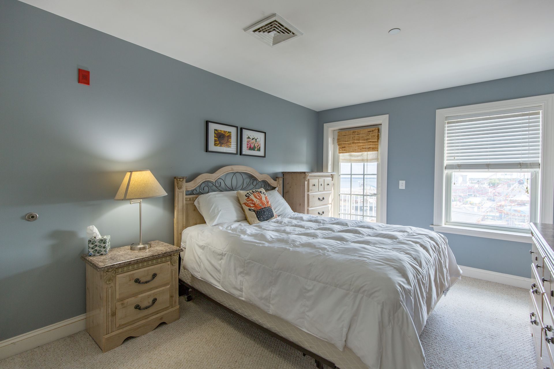 A bedroom with a bed , nightstand , dresser and two windows.