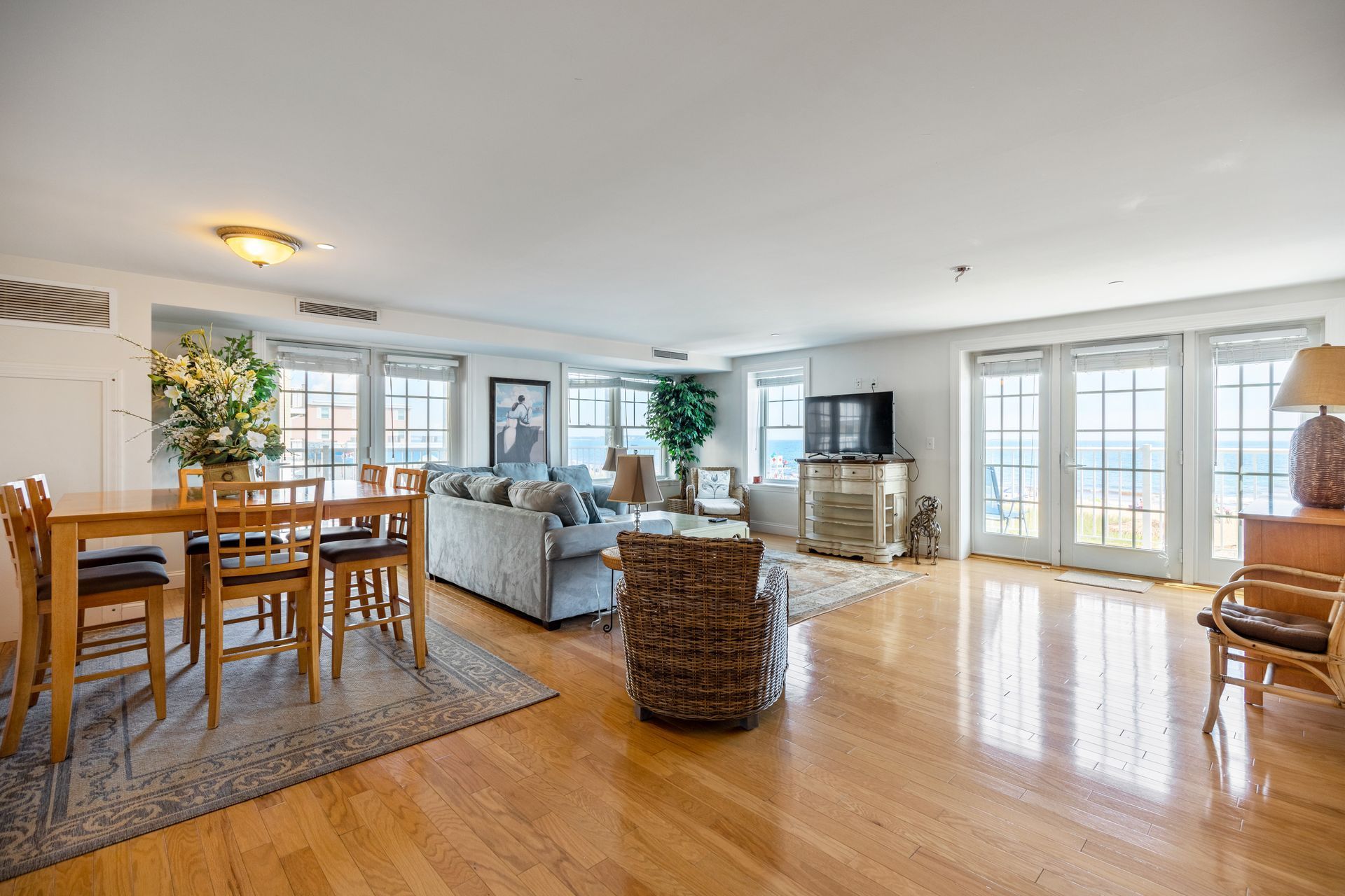 A living room with hardwood floors , a couch , chairs , a table and a television.