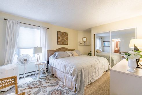 A bedroom with a large bed , dresser , chair and mirror.