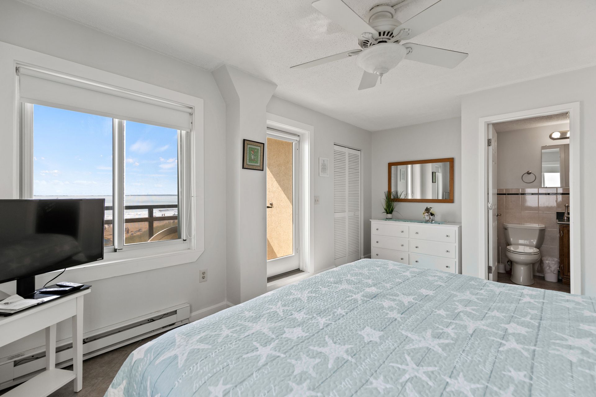 A bedroom with a king size bed , television , dresser and toilet.