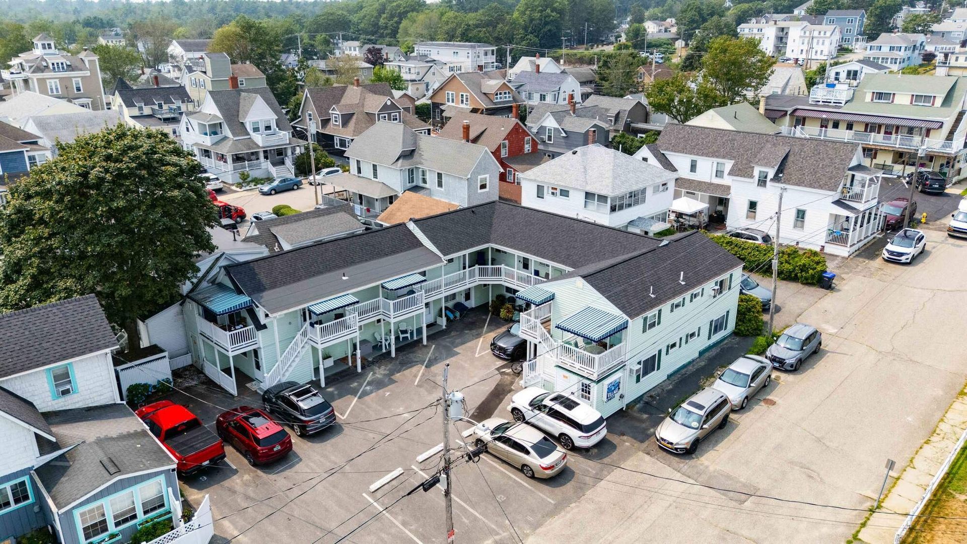Aerial view of a two-story motel with parked cars; surrounded by residential buildings and a green grassy area.