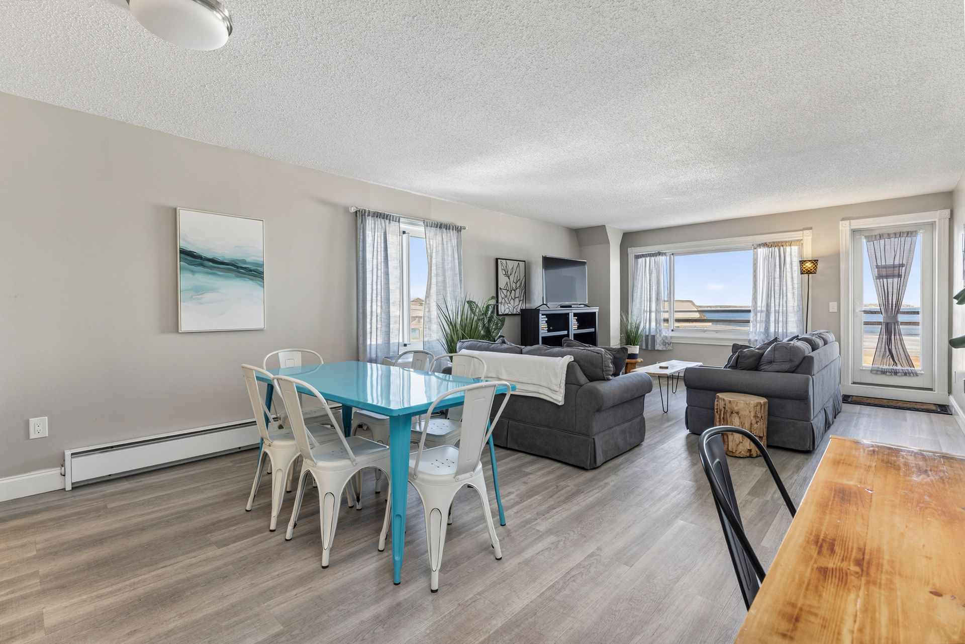 Living room with teal table and white chairs, sofa, TV, and large window.