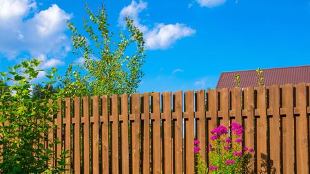 A wooden fence with flowers in front of it and a house in the background.
