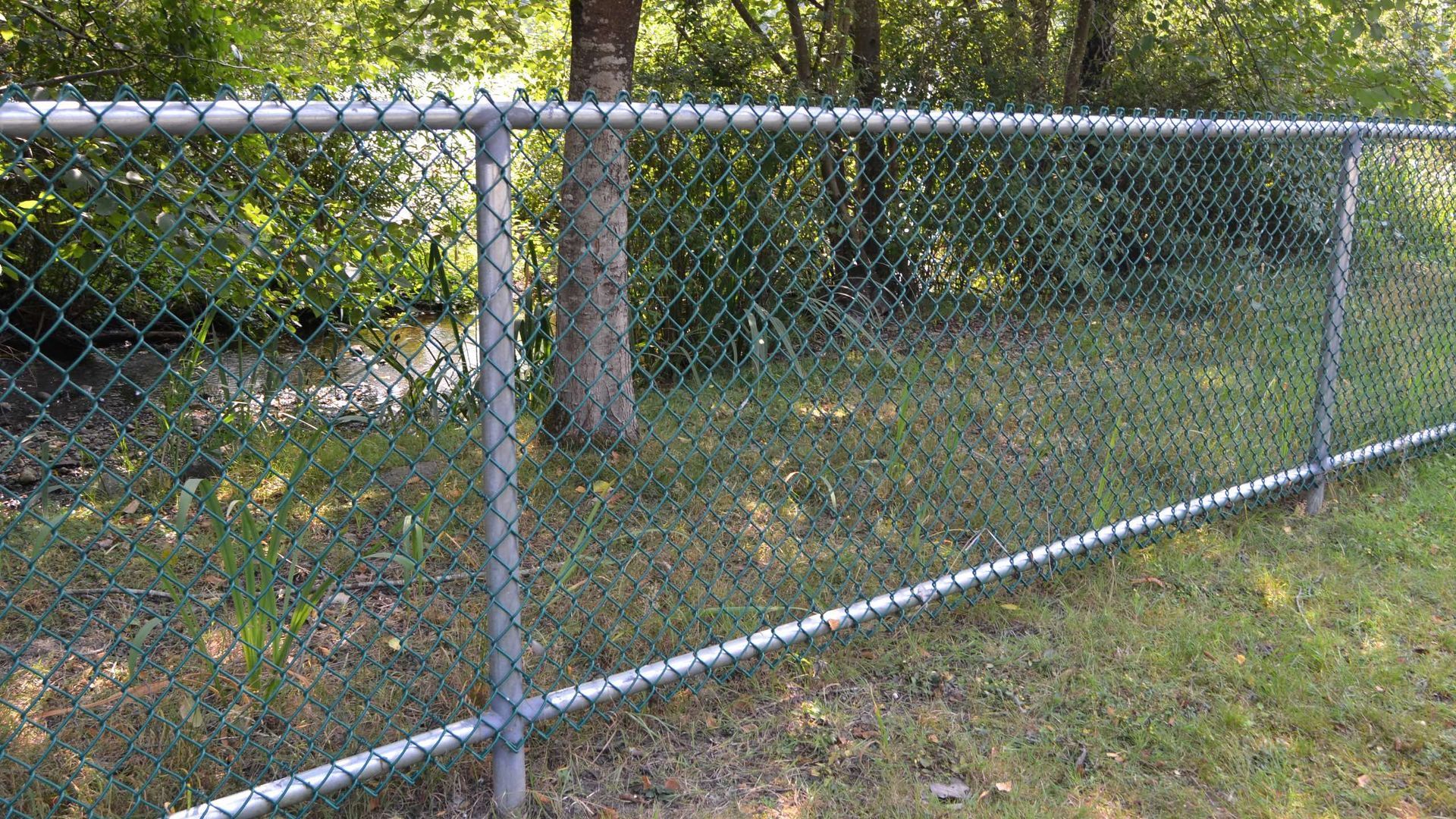 A chain link fence is sitting on top of a lush green field.