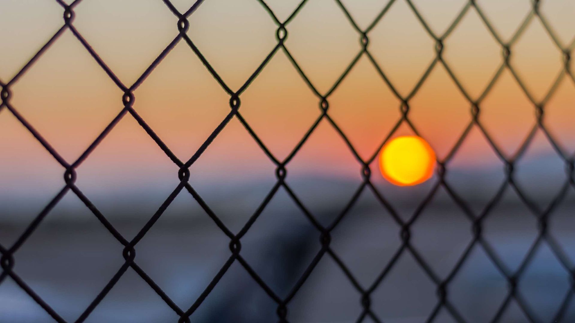 A chain link fence with a sunset in the background.