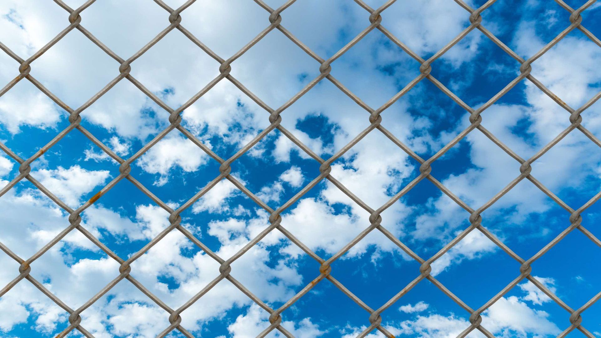 A chain link fence against a blue sky with clouds