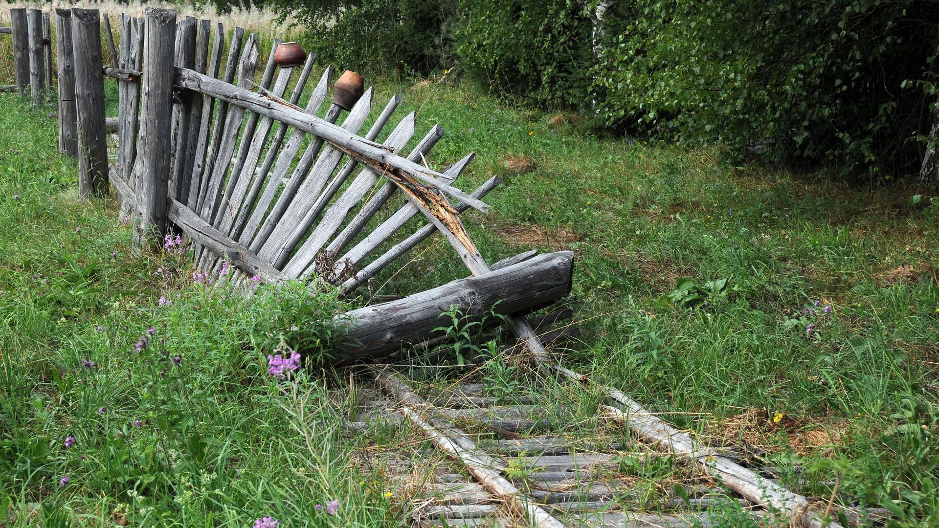 A wooden fence is sitting next to a train track in the grass.