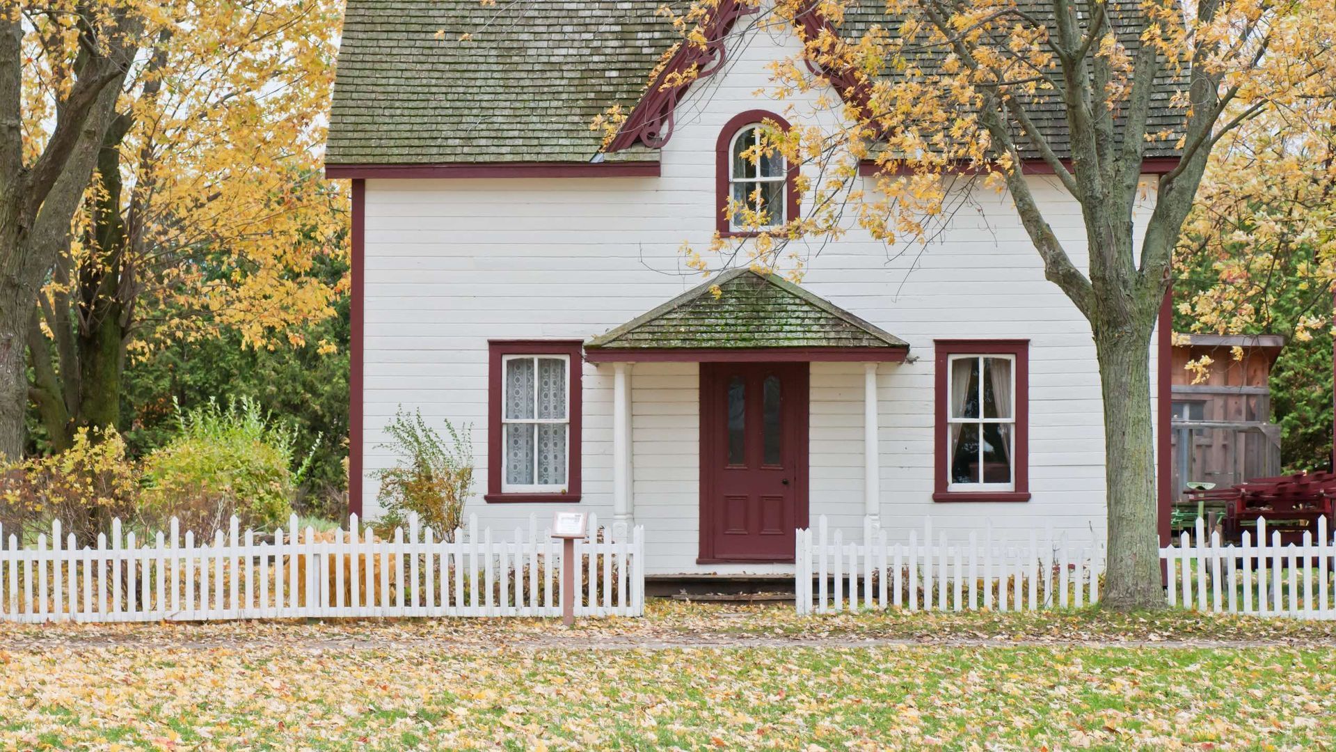 A white house with a red door and a white picket fence in front of it.