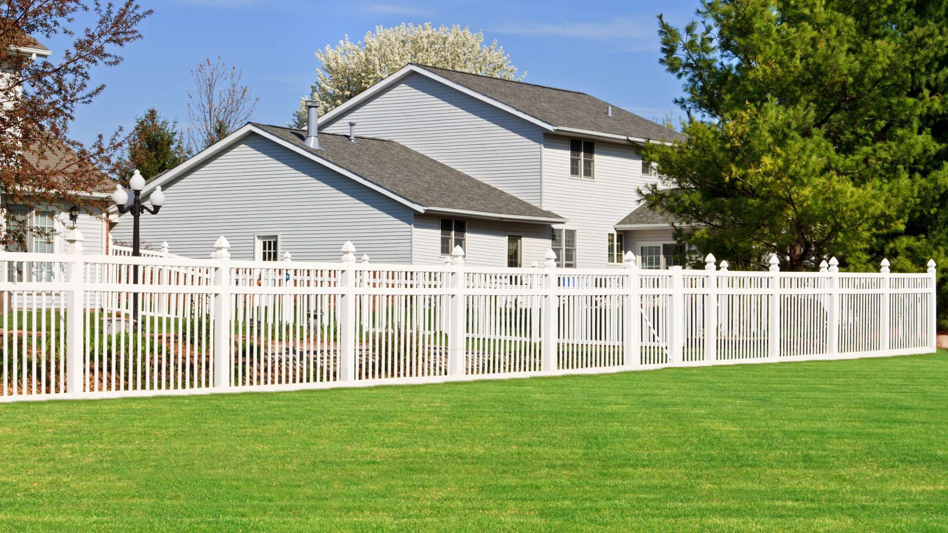 A white fence surrounds a lush green yard in front of a house.