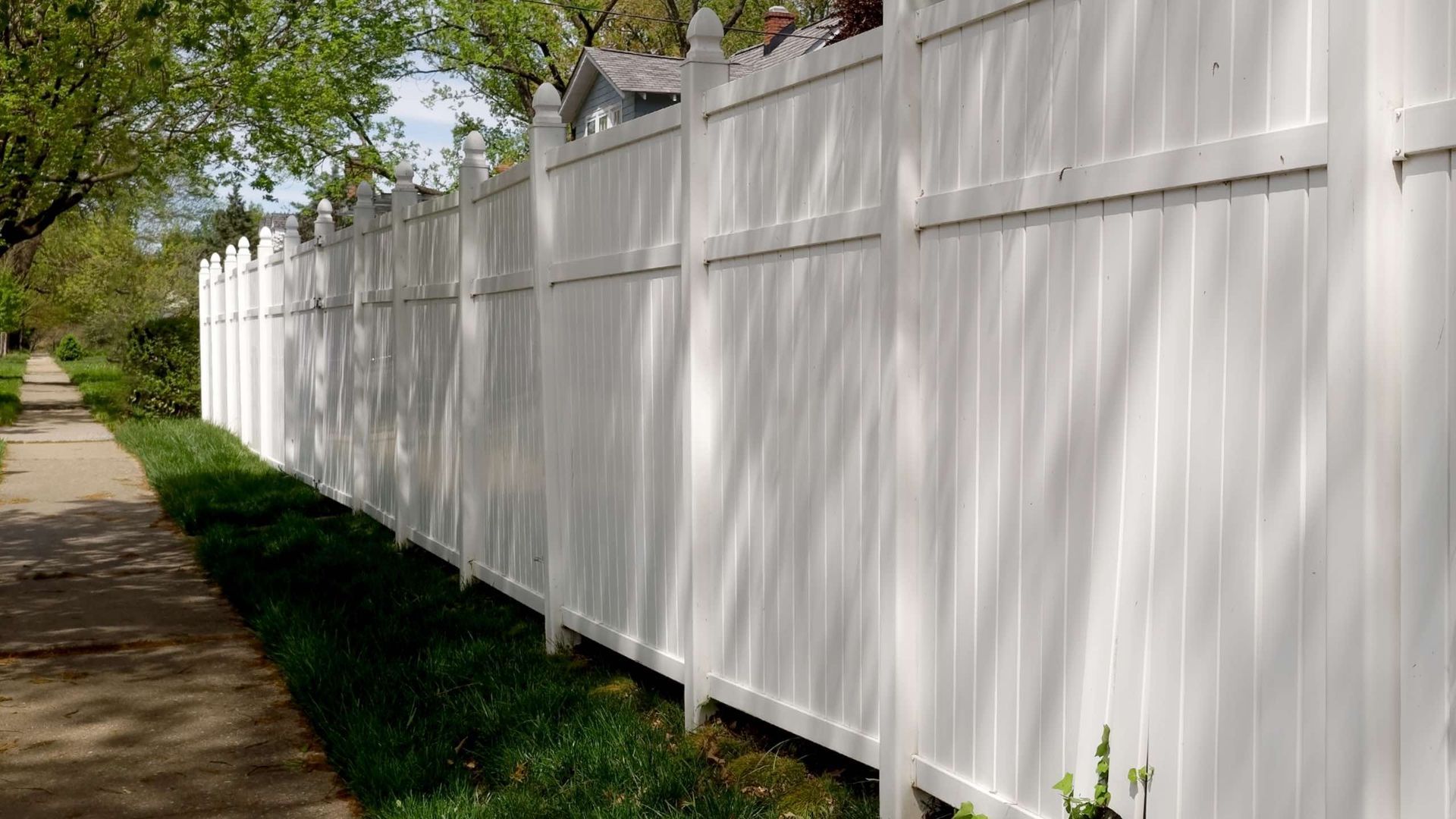 A white fence along a dirt path with trees in the background.