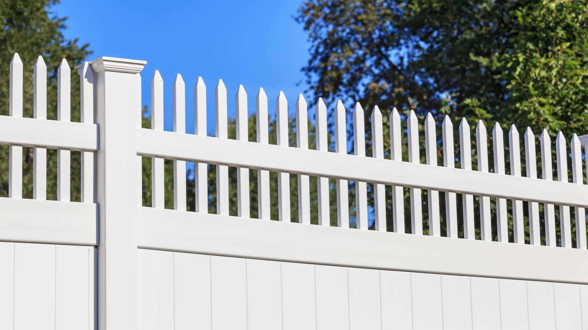 A white picket fence with trees in the background.