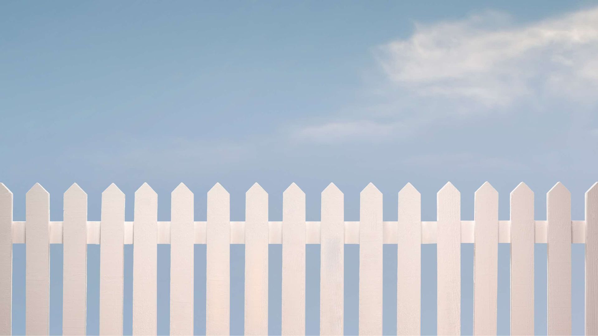 A white picket fence against a blue sky with clouds.