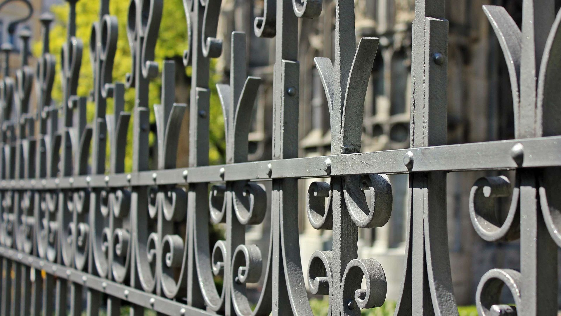 A close up of a wrought iron fence with a cemetery in the background.