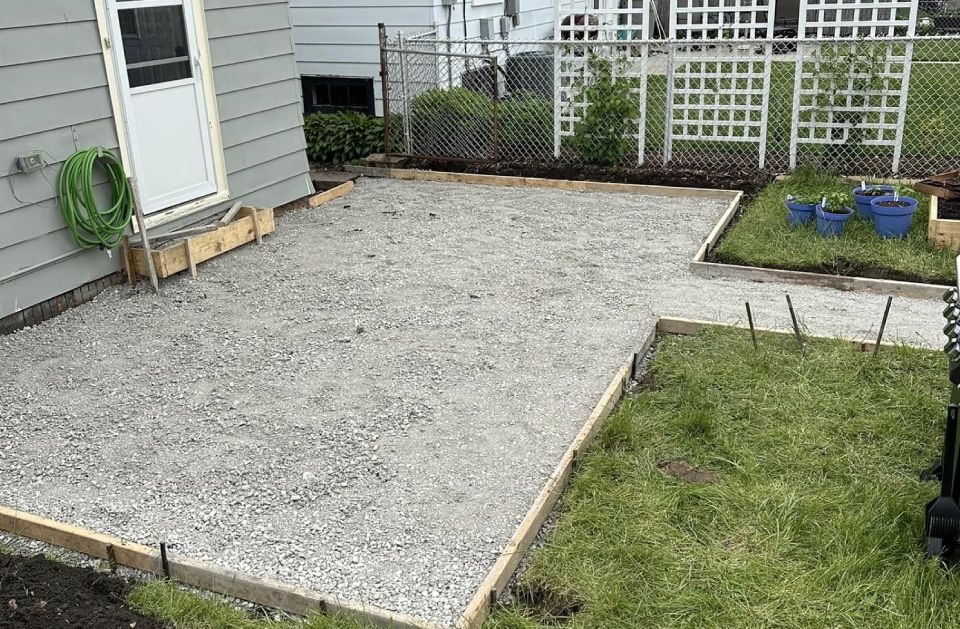 A concrete patio is being built in the backyard of a house.