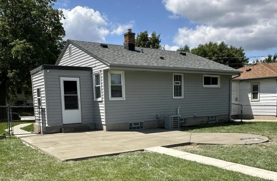A small gray house with a concrete driveway in front of it.