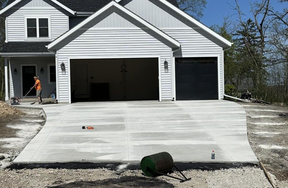 A man is cleaning a concrete driveway in front of a house.