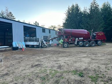 A red concrete mixer truck is pouring concrete into a dirt field in front of a building.
