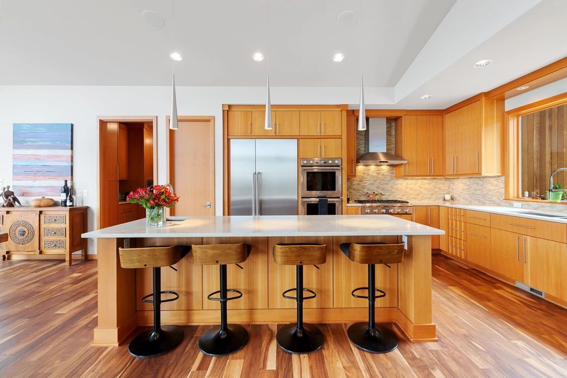 Modern kitchen with wood cabinets, island with stools, stainless steel appliances, and hardwood floors.