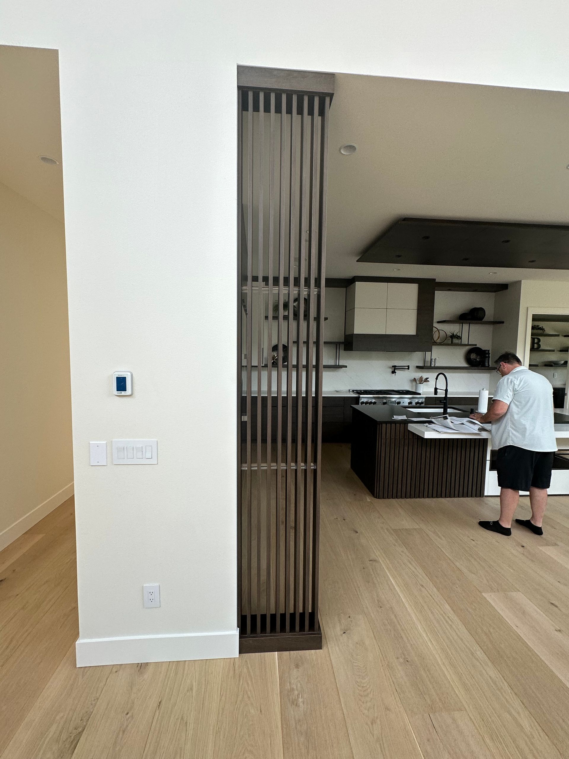 Wooden slat divider in a home's doorway, separating a hallway from a kitchen with a person at the island.